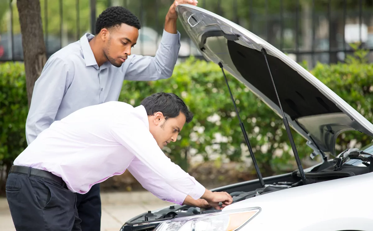 Zwei Männer in Businesskleidung beugen sich über eine geöffnete Motorhaube.